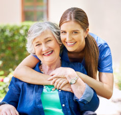 caretaker hugs the elderly woman behind